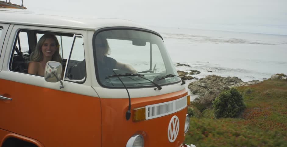 Man and woman ride in a volkswagen bus on a coastal road
