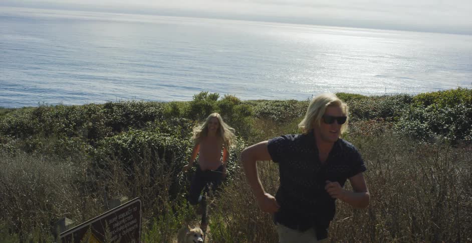 Man and woman run on a grassy beach with a dog