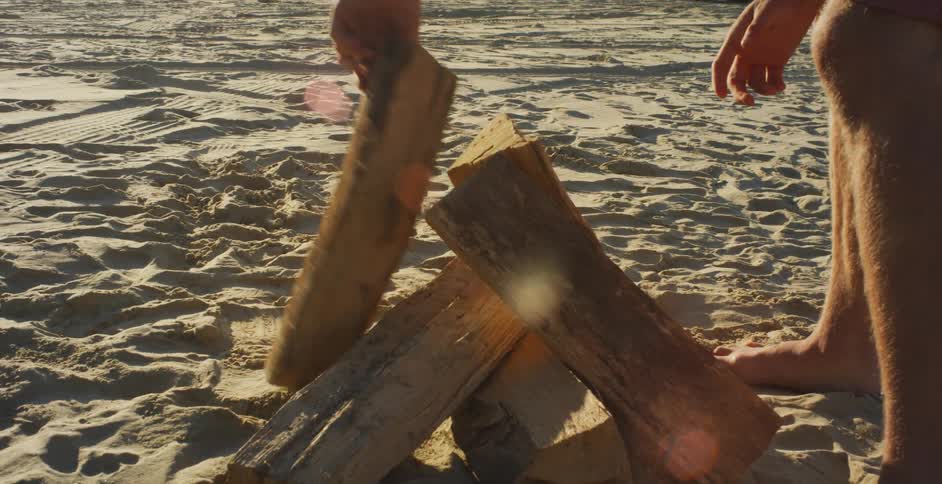 A man stacks logs on the sand for a fire