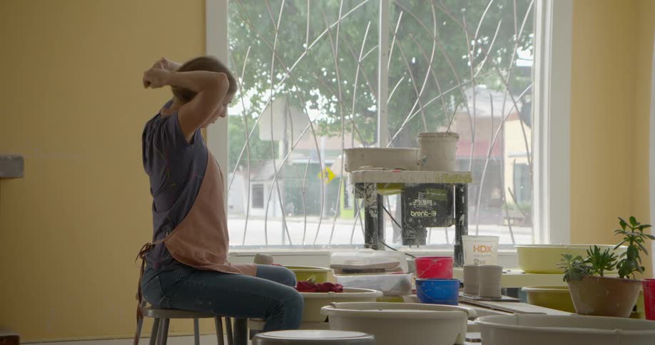 A woman ties her hair up before working on pottery