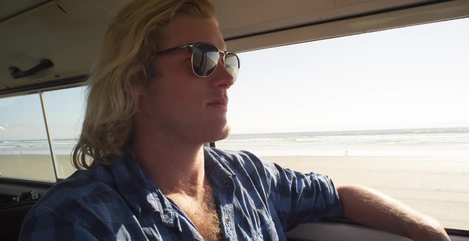 A man is smiling as he drives his vehicle on the beach on a sunny day