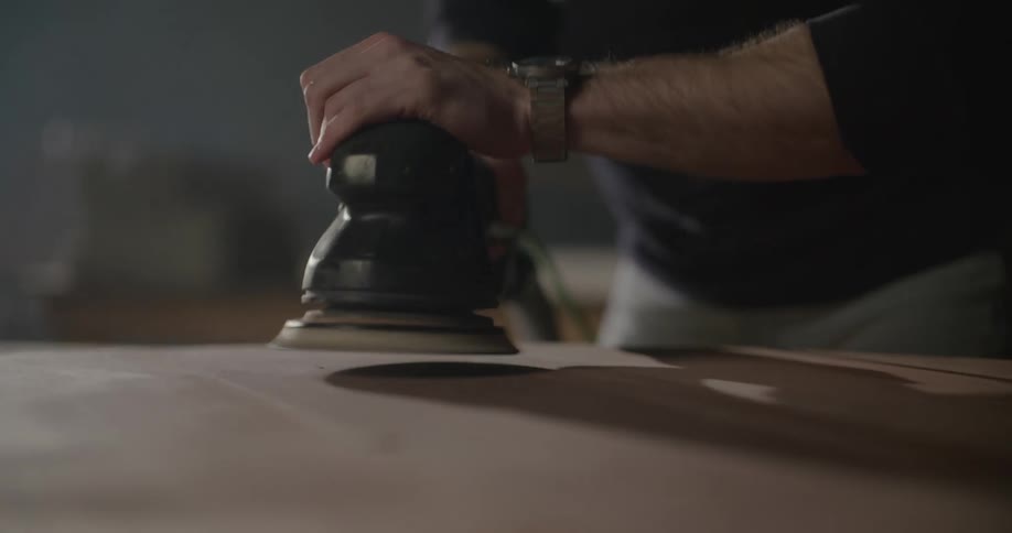 A man is using a sander on a wood surface