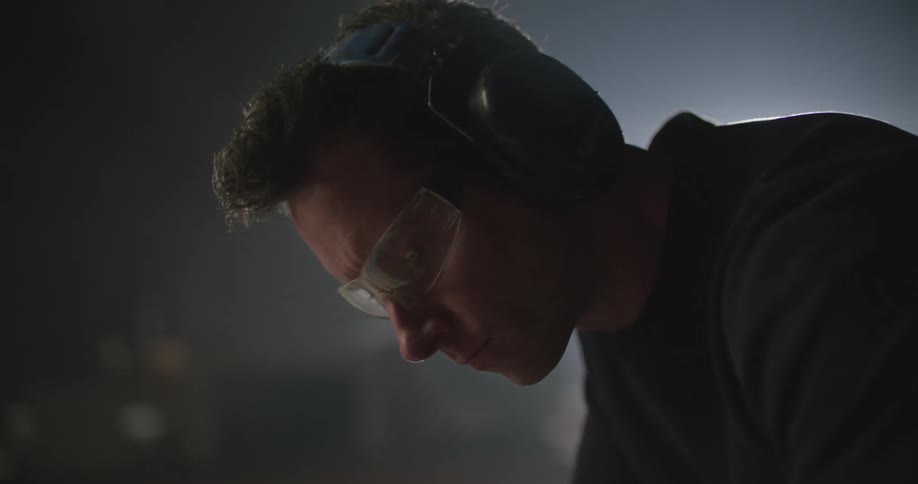 Man wearing safety goggles and ear protection works with power tool in workshop