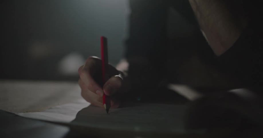 A man in a workshop writing on a piece of paper with a pencil with a light in the background
