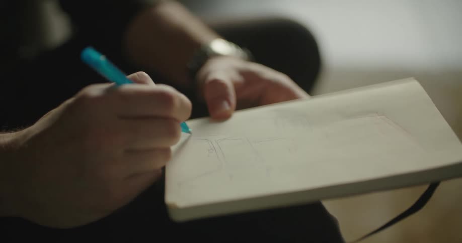 A man is sitting indoors and drawing on paper
