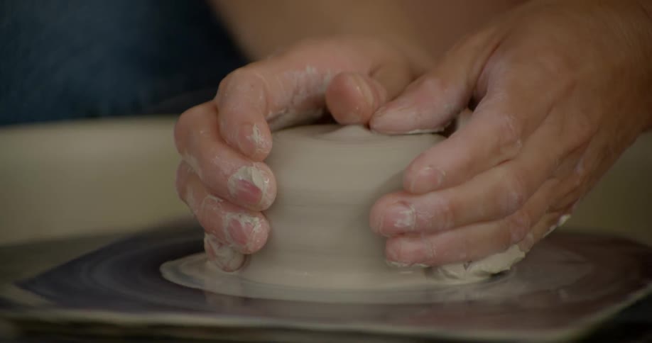 A person molds clay on a potter's wheel