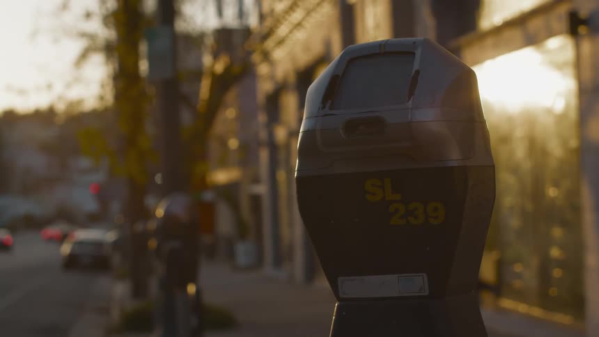 A parking meter on a city street with cars driving past