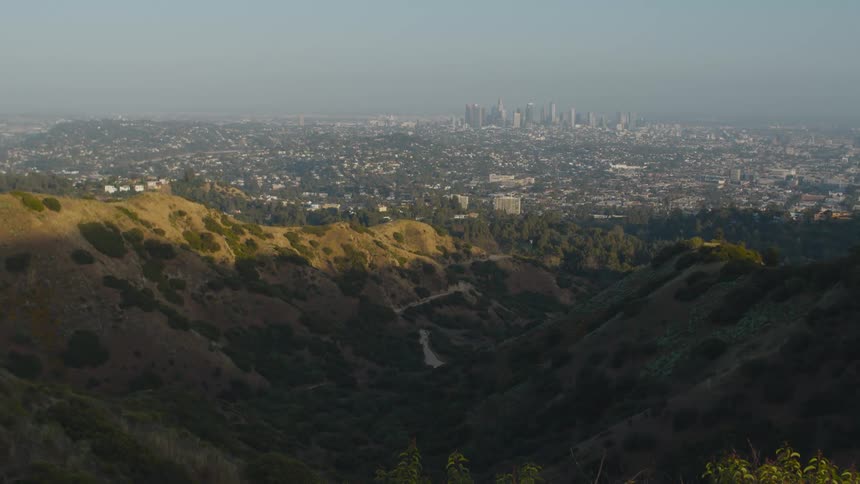 Smog obscures a city skyline in the distance from a canyon