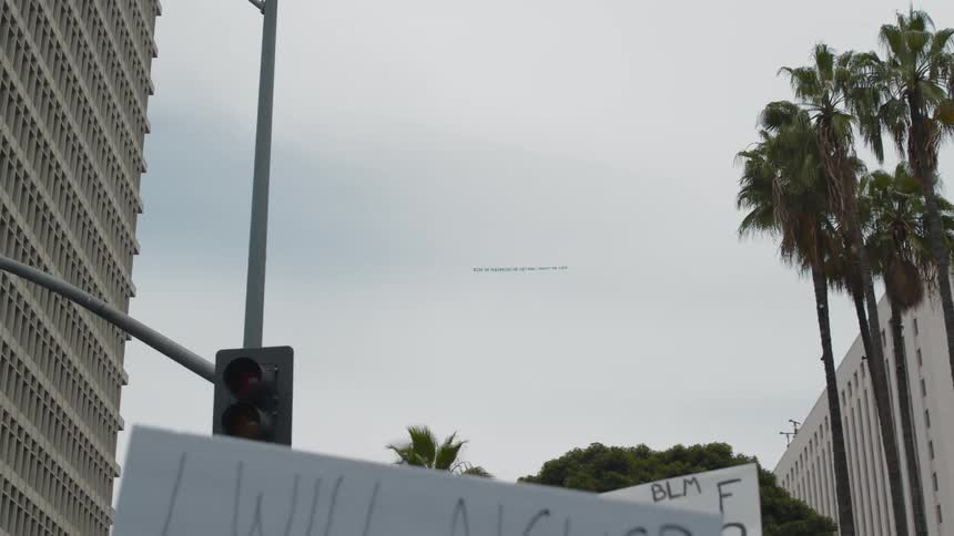 Protesters holding black lives matter signs stand near intersection under tall building