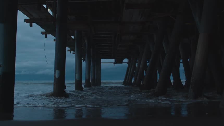 Surf flows onto beach under pier onto wet sand reflecting the pier supports