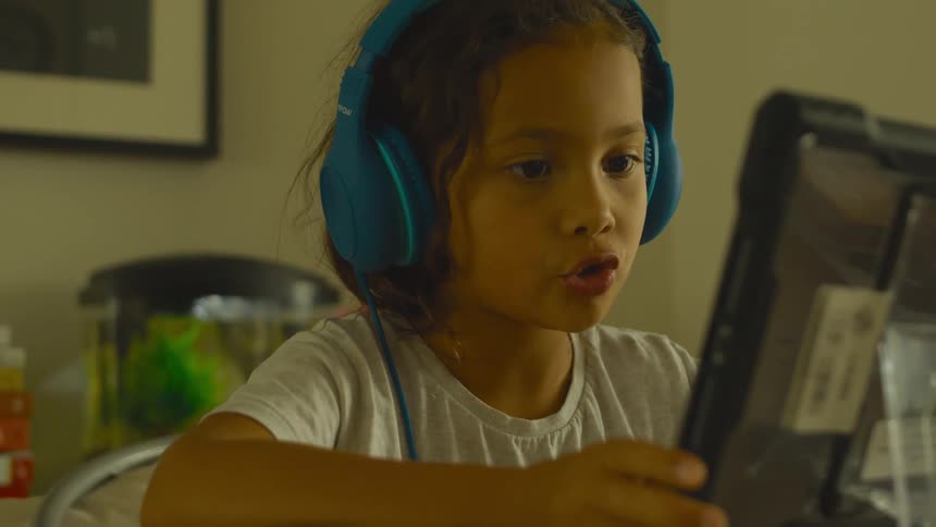 A little girl sits at home and looks at a computer