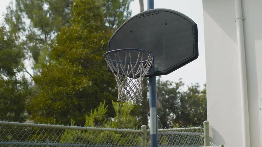 A basketball net sits near a chain link fence in a park