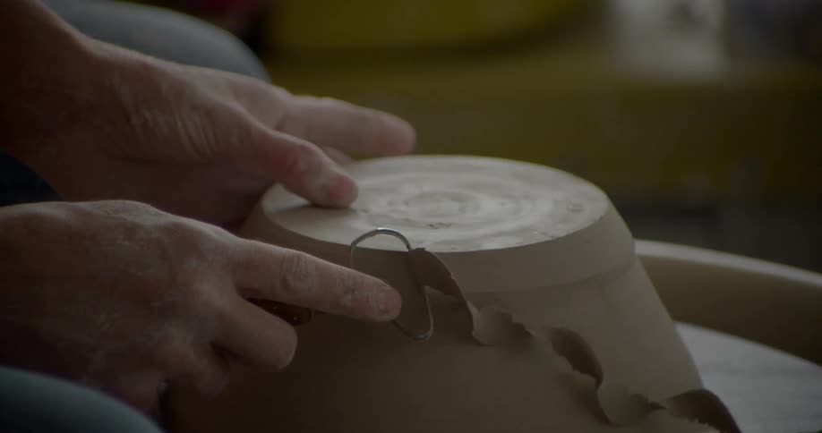 A person uses a tool on spinning clay