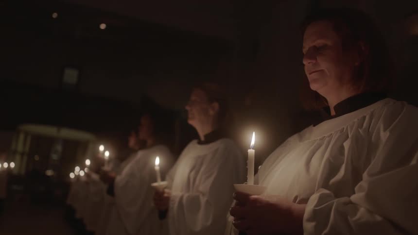 A row of people are holding candles and wearing robes