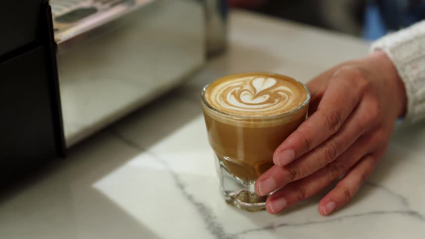 A person pushing a glass of coffee across a counter