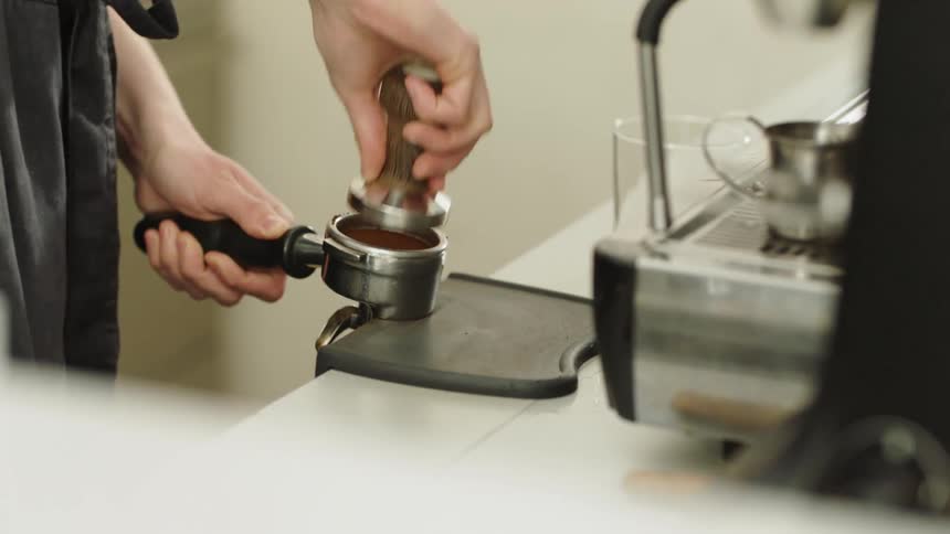 A man presses down on espresso grounds while making a drink in a cafe