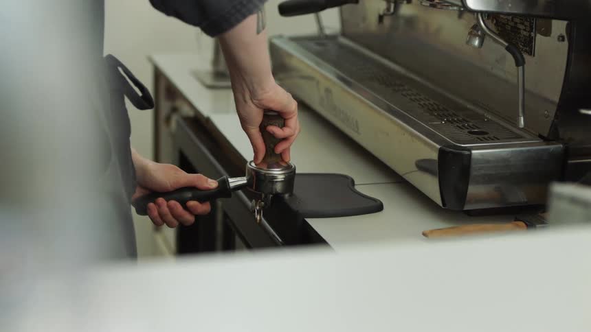 Barista pressing ground coffee into a container for a espresso machine