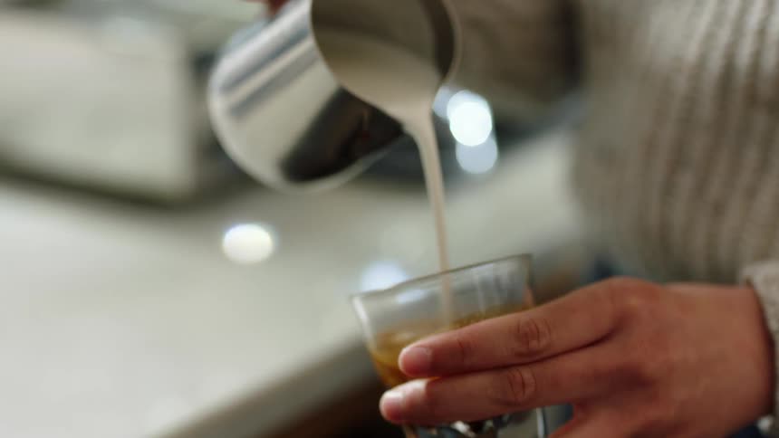 Barista mixing milk with espresso coffee on a shop