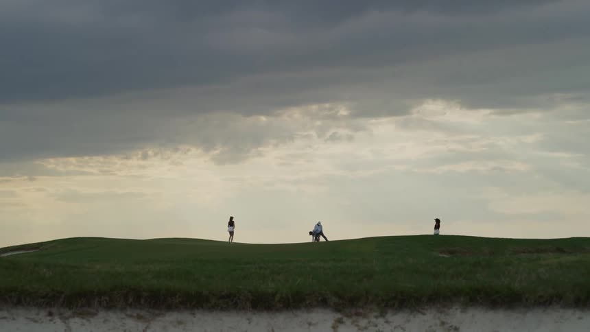 A golfer squats down before putting while three friends wait
