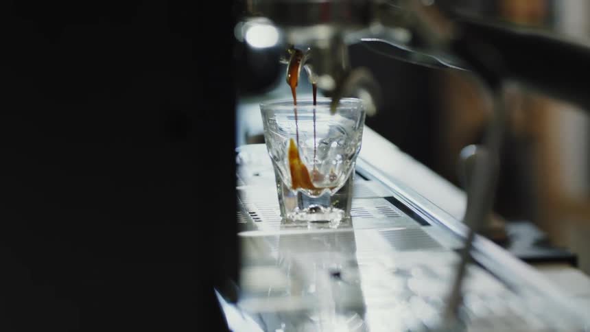 A view of coffee coming from an espresso machine into a shot glass