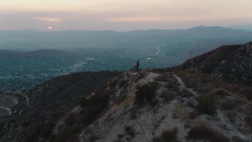 A person on a bicycle is on the top of a mountain watching the sun set over mountains in the distance