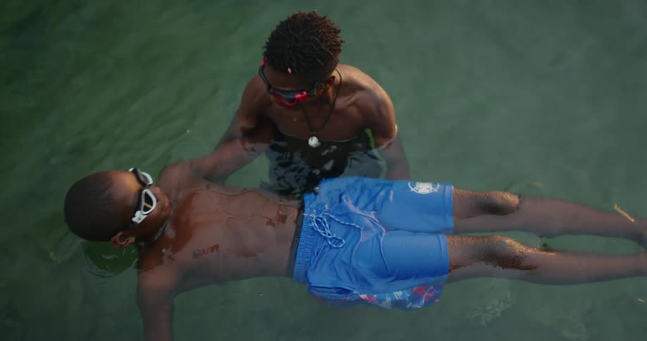 A boy holds another boy on his back learning to float in a lake