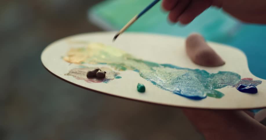 Painter mixing oil paintings over a pallet with a small brush