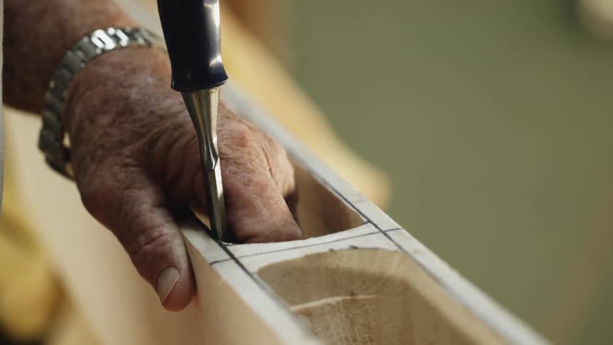 A person in a room with a wristwatch using a chisel on a piece of wood