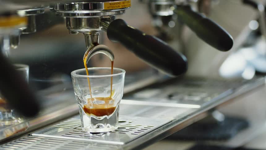 The espresso machine is filling the small glass