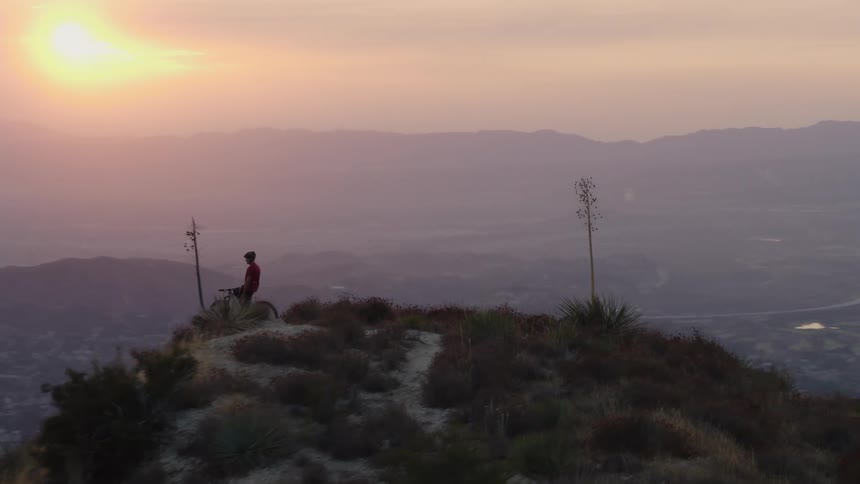 A person on a bicycle is on the top of a mountain watching the sun set over mountains in the distance