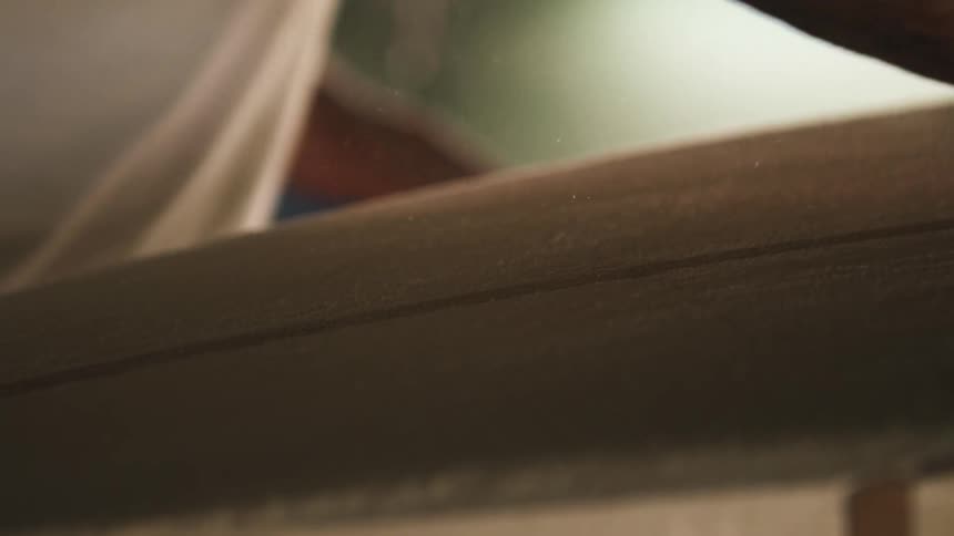 A man rubs a sanding pad along the surface of an unpainted surfboard