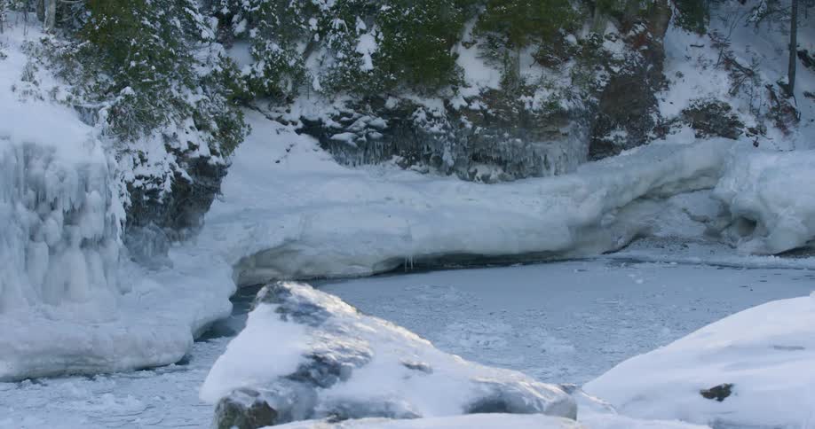 A ground with rocks covered in snow and ice with a cliff in the background