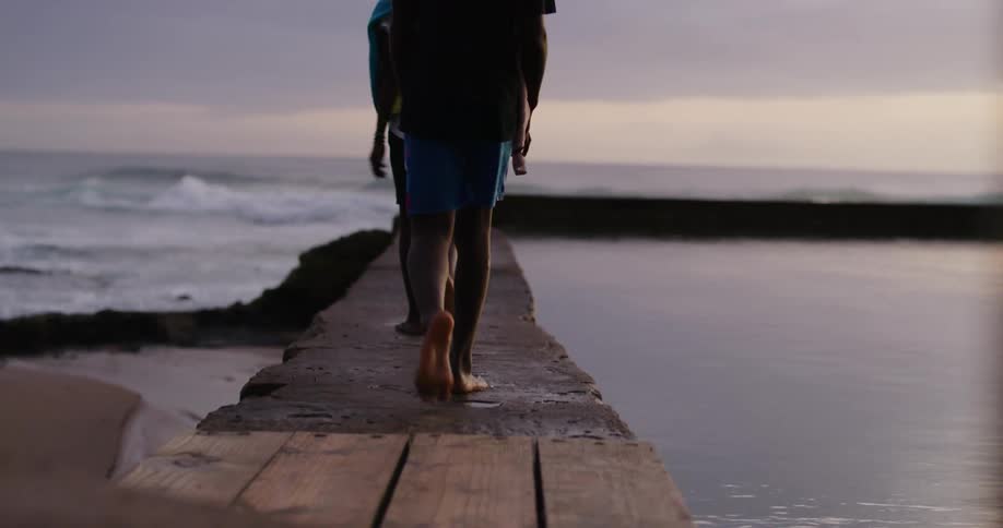 Two young boys walking over a pier in the beach at sunset