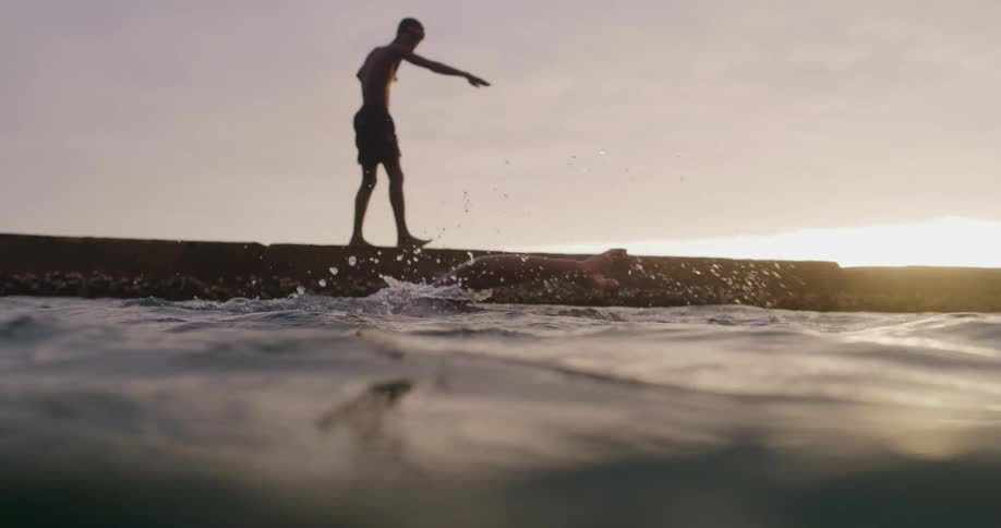 A person wearing goggles swims in the water while another person walks on the beach nearby