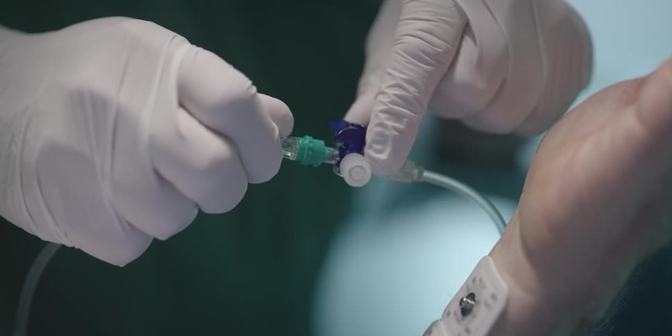 A medical professional tightens something on an iv tube coming from a patient
