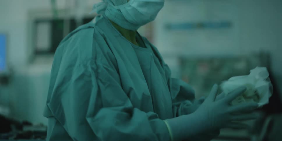A surgeon adjusts her gloves before turning and walking away in an operating room