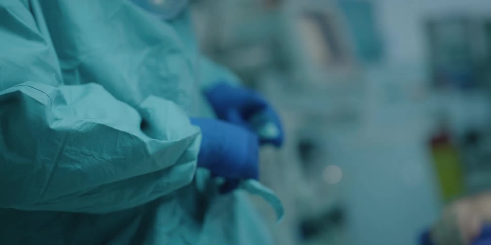 A nurse helps a doctor put gloves and his scrubs on