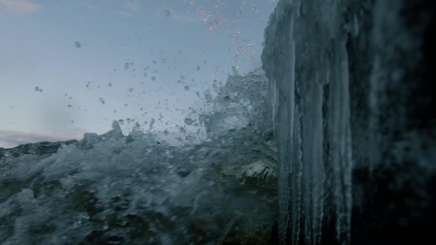 Water splashes against a wall of icicles