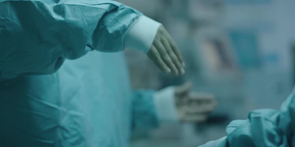 A nurse removes gloves from packaging and holds them open for a surgeon to put on