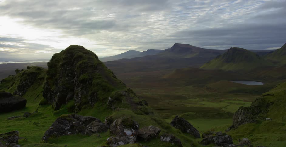 Grassland with hills and mountains and a mountain range on the horizon under a cloudy sky