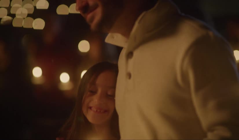 A man hugs his daughter as they stand in a crowd at a candlelight vigil