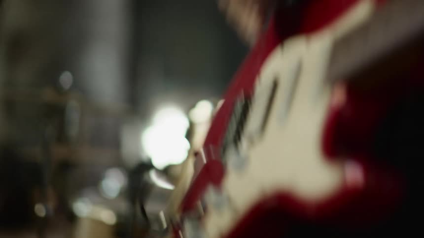 A person in a room playing a guitar with a drum set and a wall in the background