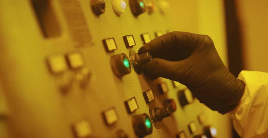 Worker wearing protective black latex gloves turns a know on a complex control board