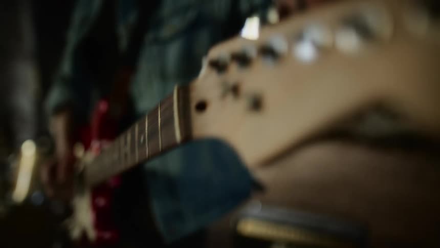 A person in a room tuning a guitar with a speaker and a drum set in the background