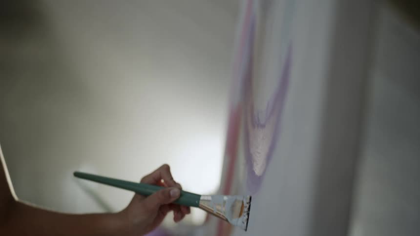 A female artist paints colorful lines on a large canvas