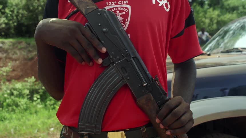 A man holds a gun in front of a vehicle