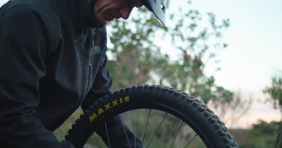 A man is working on his bicycle wheel in the woods