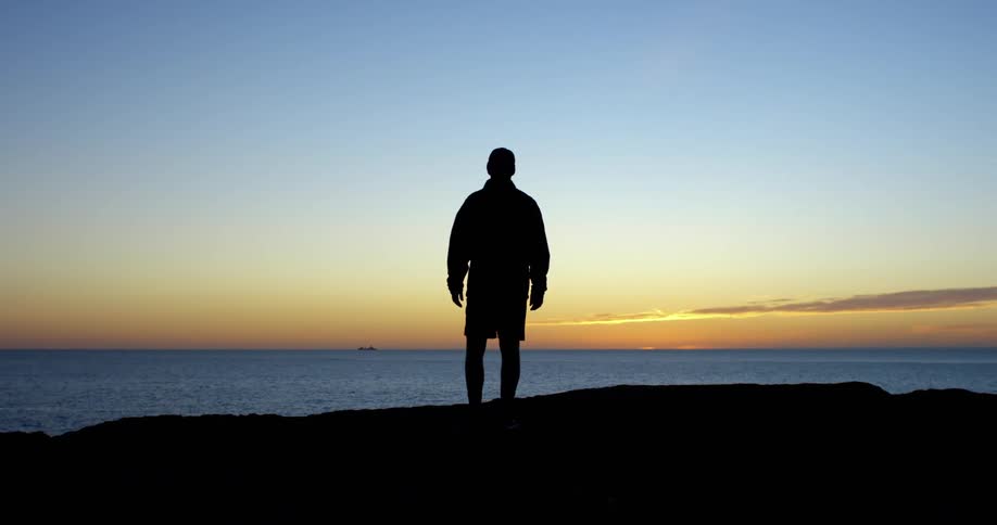 The silhouette of a man standing looking out at the ocean and golden sky