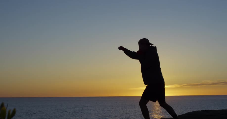 A silhouette of a man shadowboxing with the ocean the sunset the sky and clouds in the background