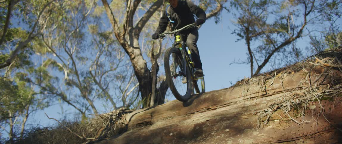 A cyclist rides down a steep slope in a woodland during the day